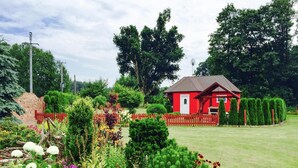 Ein rotes Haus, umgeben von einem gepflegten Garten mit verschiedenen Pflanzen und einem roten Holzpünktchenzaun.