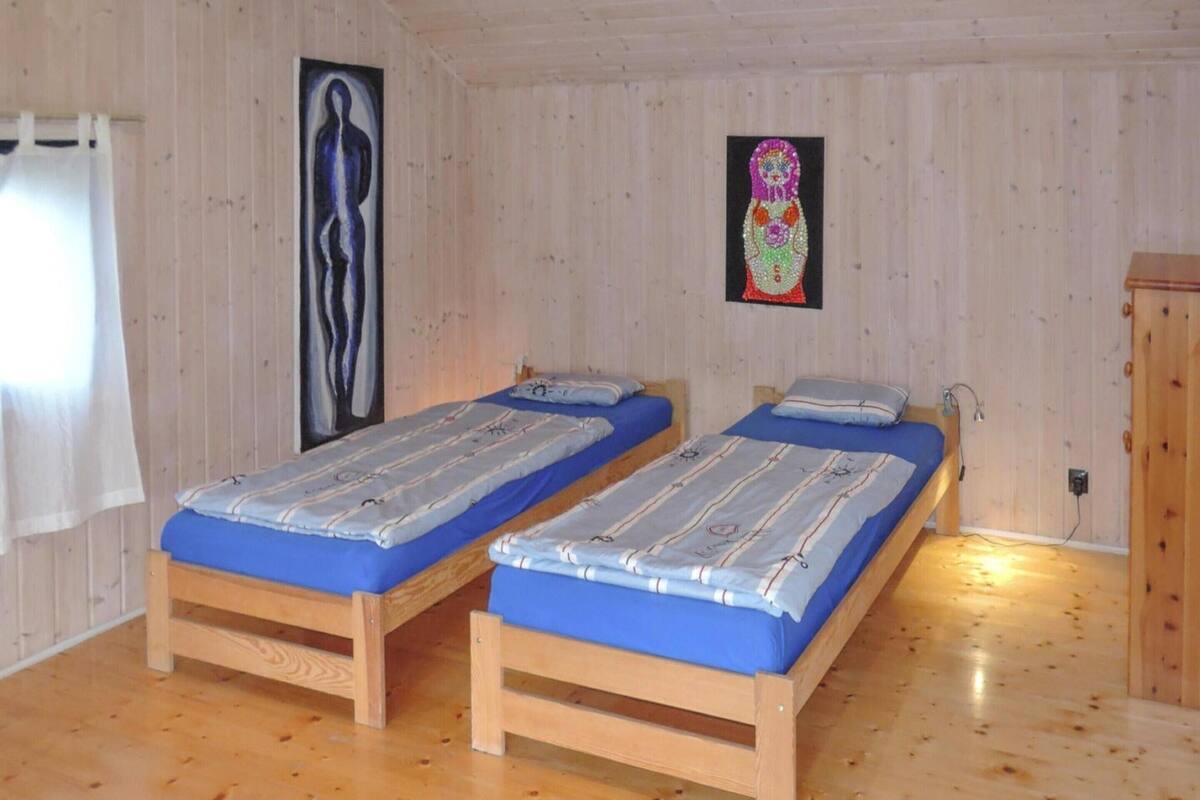 Huoneessa on kaksi puista sänkyä, joissa on siniset vuodevaatteet, puulattia ja puinen seinä, jossa on kaksi kehystettyä taideteosta.