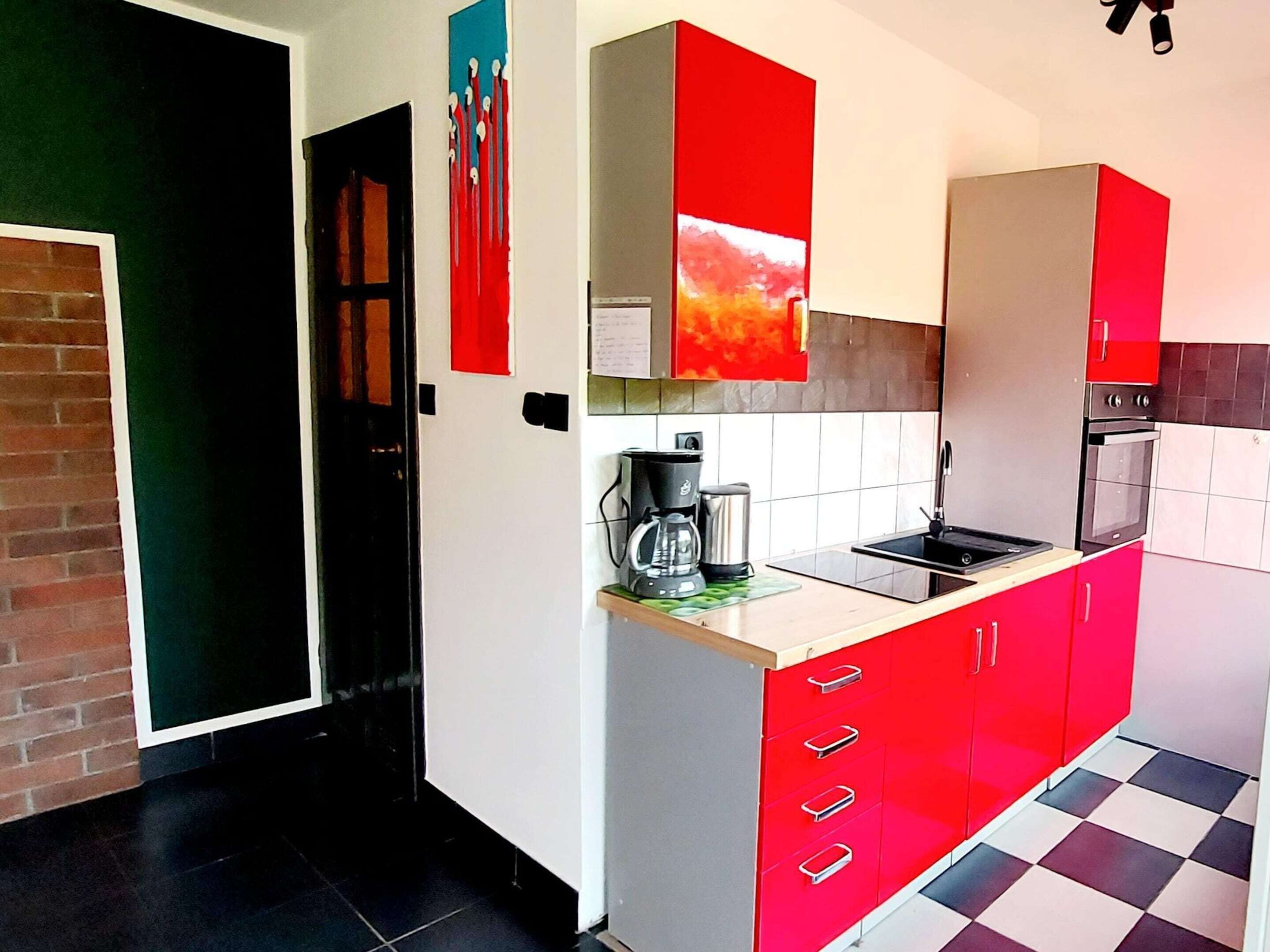 A modern kitchen with red cabinets, a black countertop, and a checkered floor.