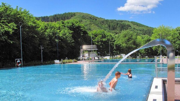 A swimming pool with clear blue water, surrounded by lush green trees and a hilly landscape in the background. - Beautiful Holiday Home in Waxweiler With Pool (Waxweiler)