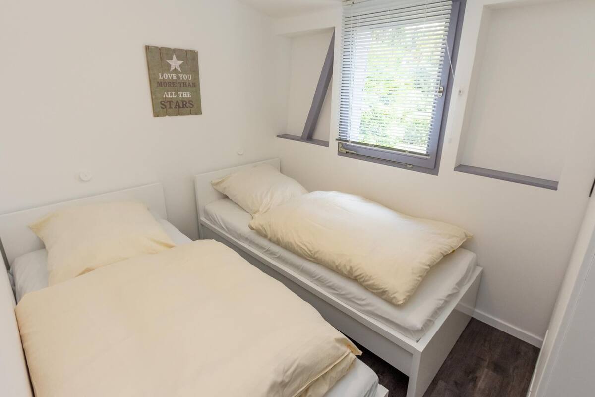 Un petit logement composé d’une seule pièce, avec deux lits, une fenêtre avec des stores et un panneau fixé au mur.