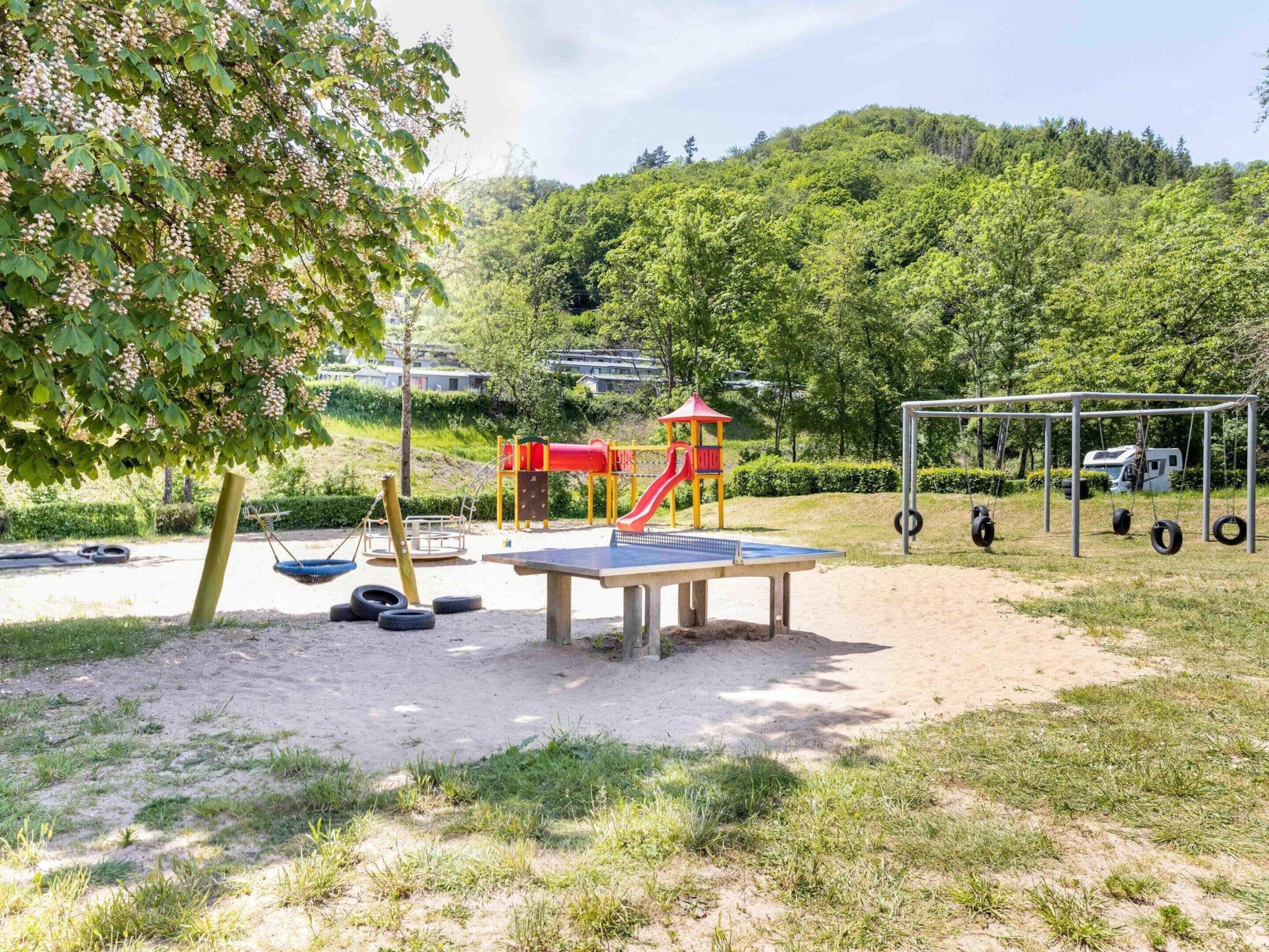 A playground with a slide, swings, and a table tennis table.