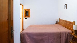 Ένα δωμάτιο με ένα κρεβάτι, ένα ξύλινο προσκέφαλο, ένα κομοδίνο με ένα φωτιστικό και μια πόρτα.