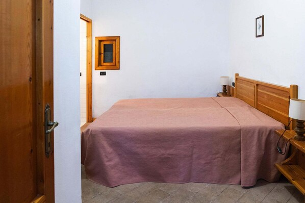 Une pièce comprenant un lit, une tête de lit en bois, une table de chevet avec une lampe et une porte.