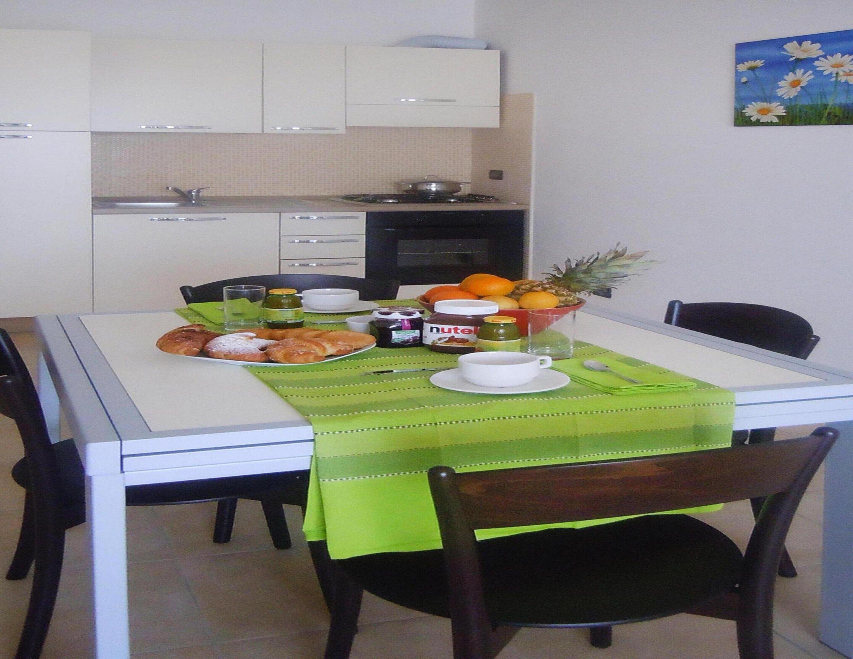A dining area with a table set for two, featuring a green tablecloth, plates of food, and a fruit bowl.