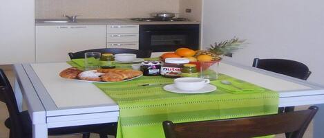 A dining area with a table set for two, featuring a green tablecloth, plates of food, and a fruit bowl.