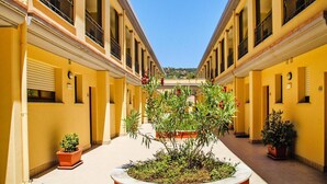 Ein Innenhof mit gelben Gebäuden, ein zentraler Garten mit Pflanzen und ein klarer, blauer Himmel.
