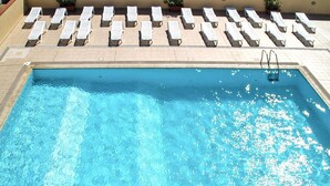 Ein rechteckiger Pool mit klarem, blauem Wasser, umgeben von weißen Liegestühlen und einer Poolanlage mit Pflanzen in Töpfen.