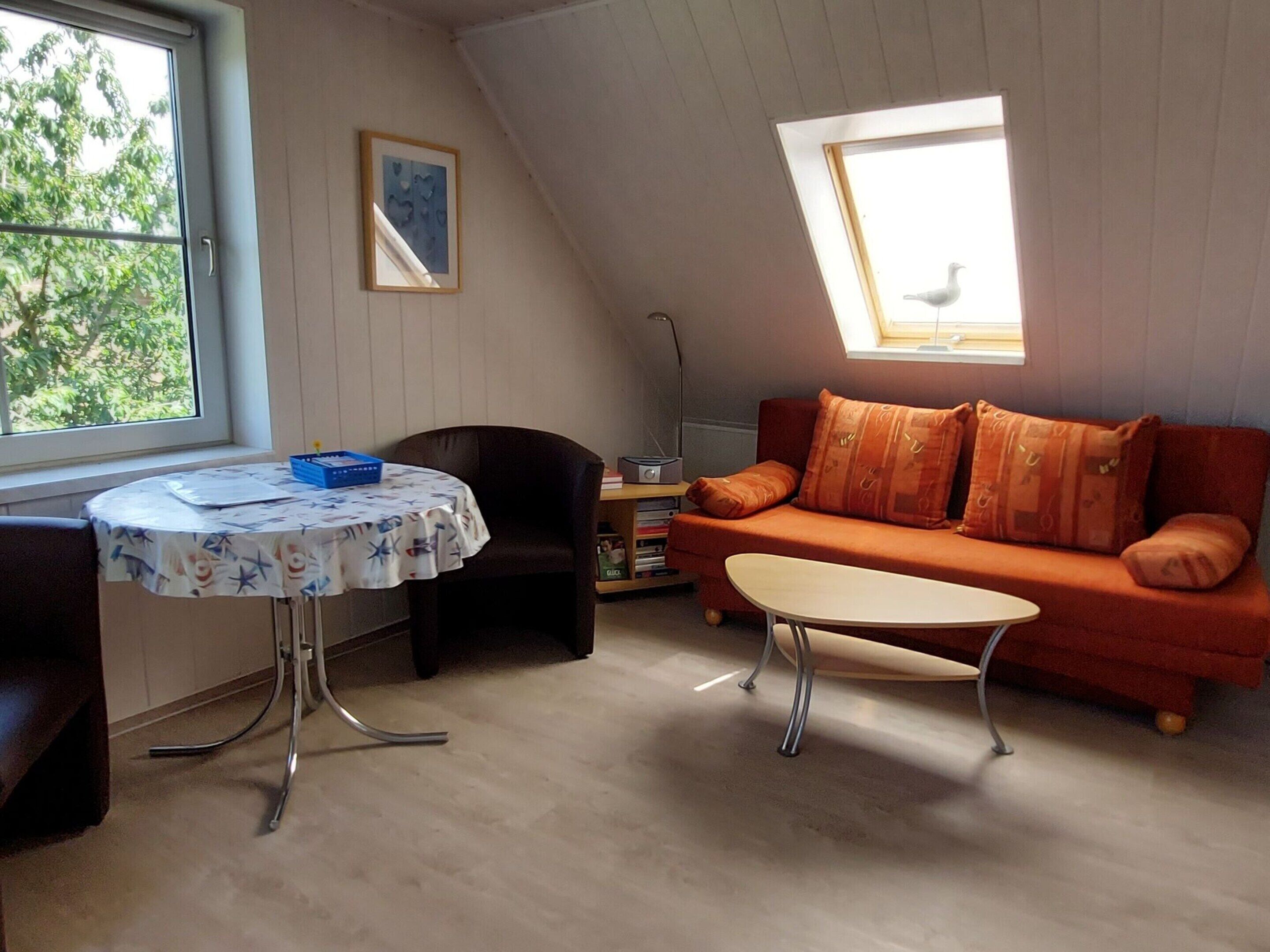 Et hyggeligt værelse med skråvægge, en sofa, et bord og en reol.