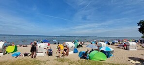 A beach with multiple tents and umbrellas, people swimming, and a clear sky. - Ferienunterkunfte - Komfortabel und in Strandnahe (Zierow)