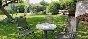 Ein Garten mit einem runden Tisch und vier Stühlen, umgeben von einer grünen Rasenfläche und verschiedenen Pflanzen.