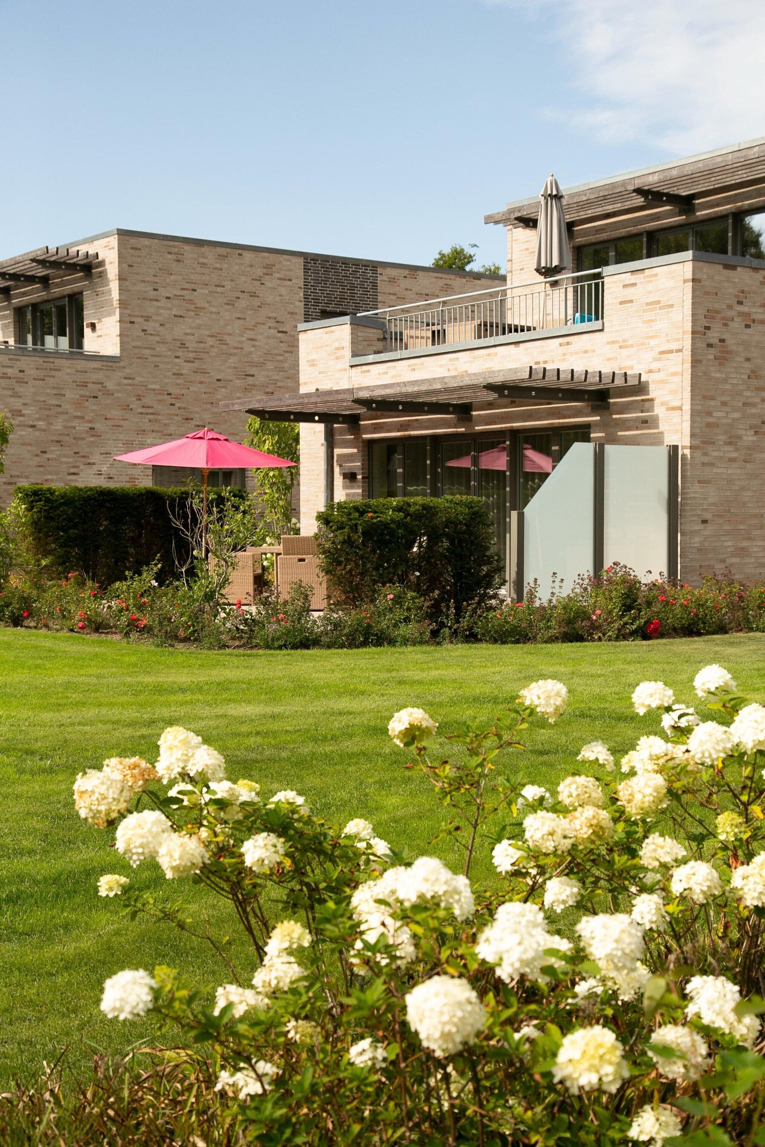 A modern house with a brick exterior, a balcony, and a well-maintained garden with white flowers.