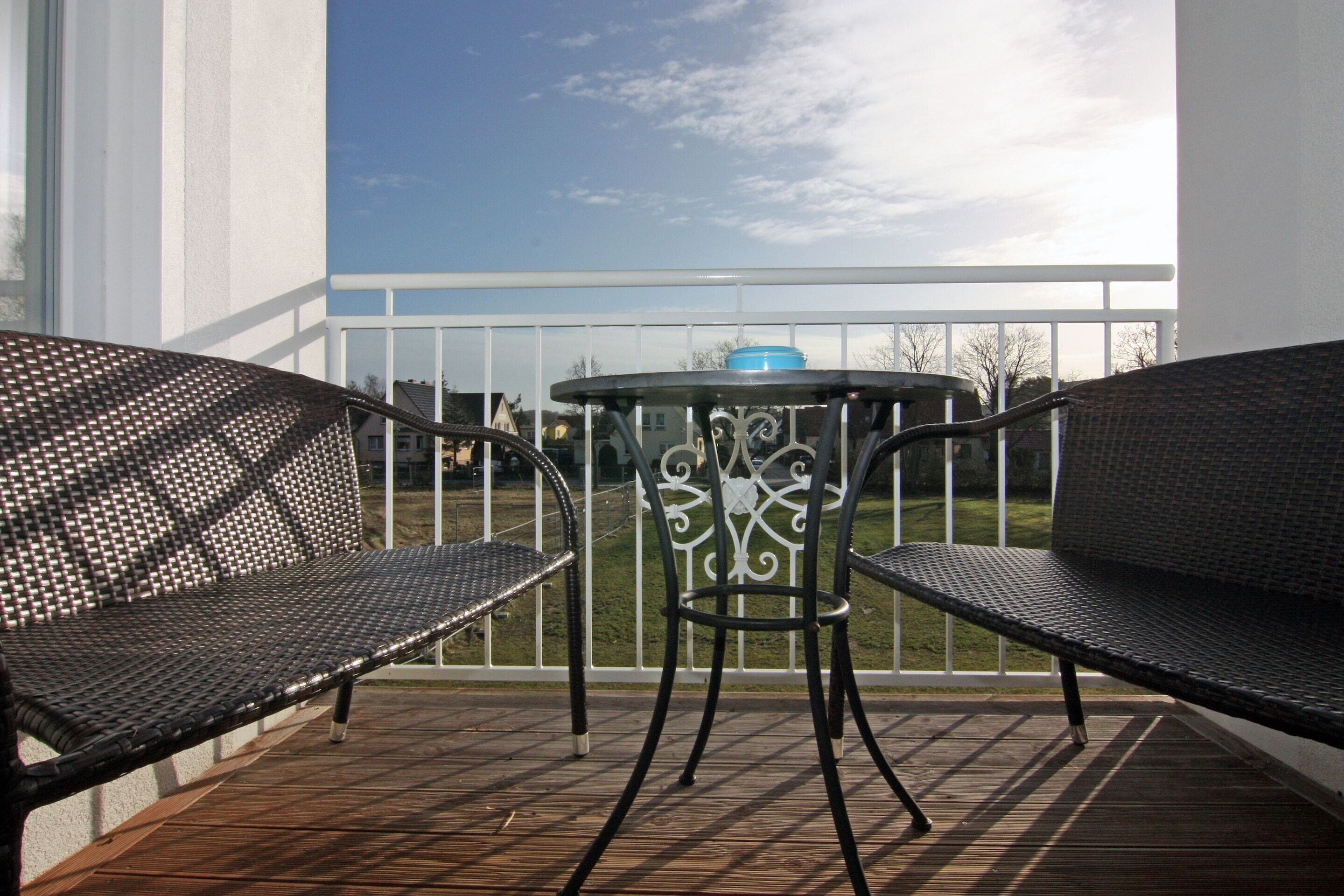 A balcony with two black wicker chairs and a small round table with a blue bowl.