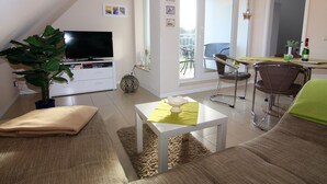 Un soggiorno moderno con televisione a schermo piatto, un divano, un tavolo da pranzo e un balcone con una sedia.