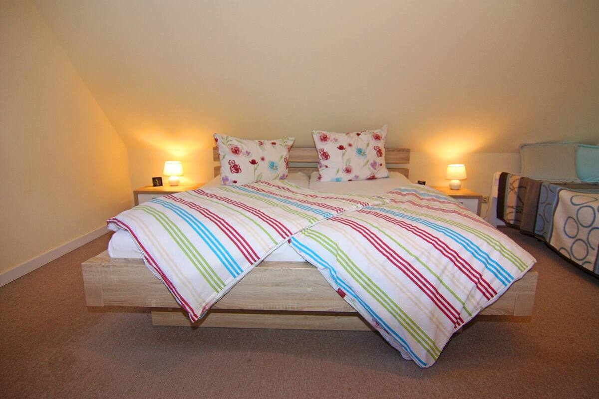 A bed with a striped bedspread and two pillows, two bedside lamps, and a headboard.