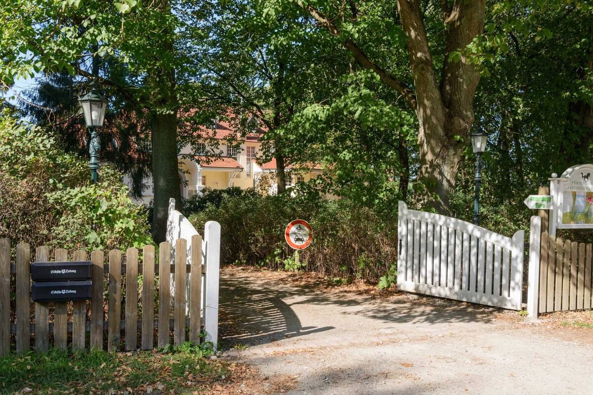 A gated entrance with a no-entry sign, a wooden fence, and a path leading to a building with a red-tiled roof.