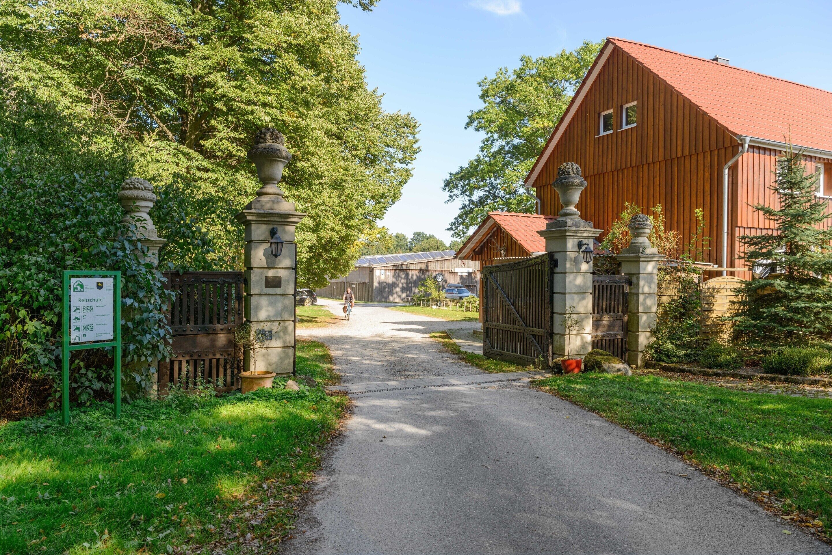 A gated entrance with a pathway leading to a building with a red roof.