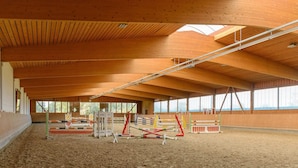 Una arena ecuestre cubierta con vigas de madera, suelo de arena y diversos obstáculos para saltar.