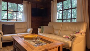 Una sala de estar acogedora con techo de madera, dos sofás de cuero, una mesa de centro con revistas y ventanas grandes con cortinas.