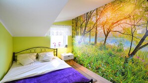 Une chambre à coucher comprenant un lit, une table de chevet, une fenêtre donnant sur un jardin et une fresque représentant des arbres et des fleurs sur le mur.