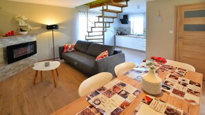 Un salon moderne doté d’une cheminée, d’un canapé, d’une table à manger avec un set de table sur le thème du café, et d’un escalier menant à un niveau supérieur.