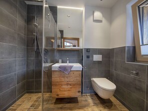 Une salle de bain moderne avec une douche à parois de verre, un meuble-lavabo en bois, un lavabo blanc et des toilettes.