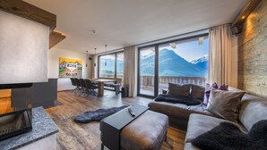 Ein modernes Wohnzimmer mit Kamin, einer Couch, einem Couchtisch und einem Essbereich mit Blick auf Berge.