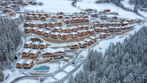 Ein schneebedecktes Resort mit mehreren Chaletgebäuden, einem zentral gelegenen Pool und umliegenden bewaldeten Gebieten.