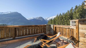 Eine Holzterrasse mit Liegestühlen und einer Steinmauer, mit Blick auf ein Gebirge.