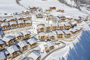 Une station de ski enneigée, composée de plusieurs bâtiments en bois disposés de manière compacte et entourée d’un paysage également recouvert de neige.