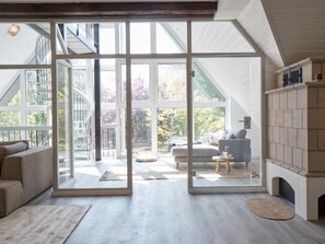 A spacious living room with a large sliding glass door leading to a balcony, a fireplace, and a view of the outdoors. - Cottage With a Fireplace Just 10 Minutes From the Beach (St. Peter-Ording)