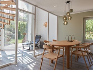 Ein moderner Essbereich mit Holztisch und -stühlen, großen Fenstern und einer Treppe.