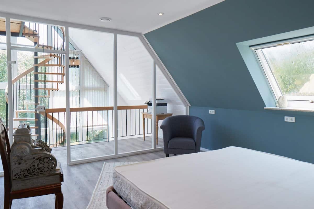 A bedroom with a bed, a chair, a desk, and a large window.