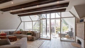 Un vaste espace de vie doté d’une grande porte-fenêtre donnant sur un balcon, de poutres en bois au plafond et d’une cheminée.