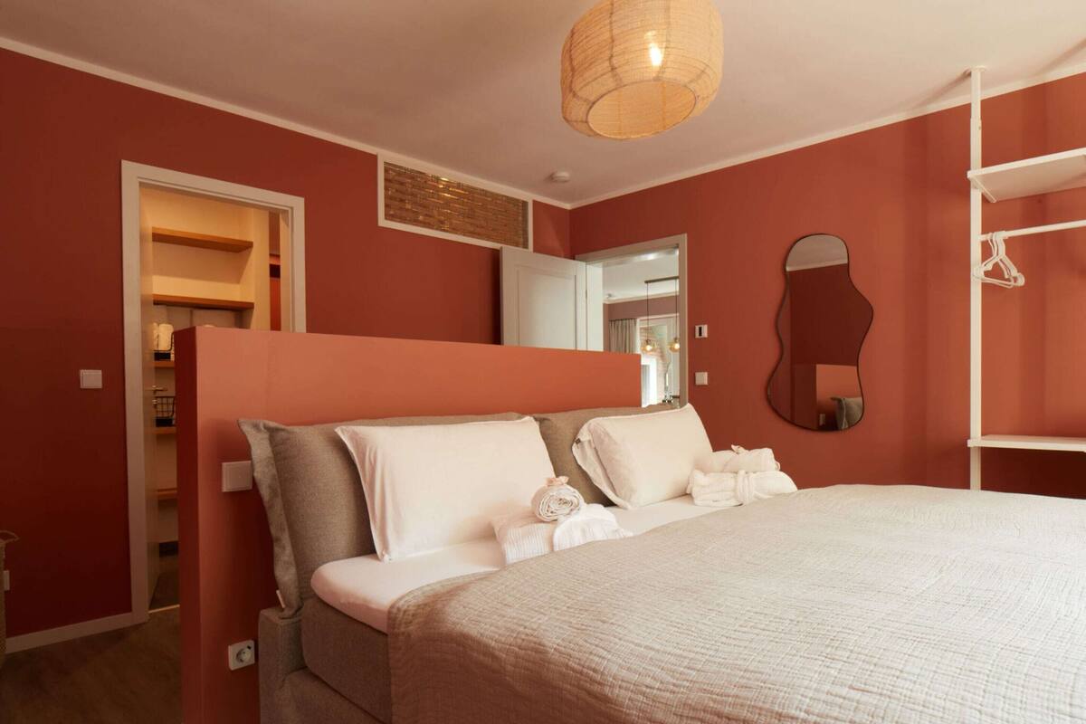 A bedroom with a large bed, a wardrobe, a mirror, and a hanging light fixture.