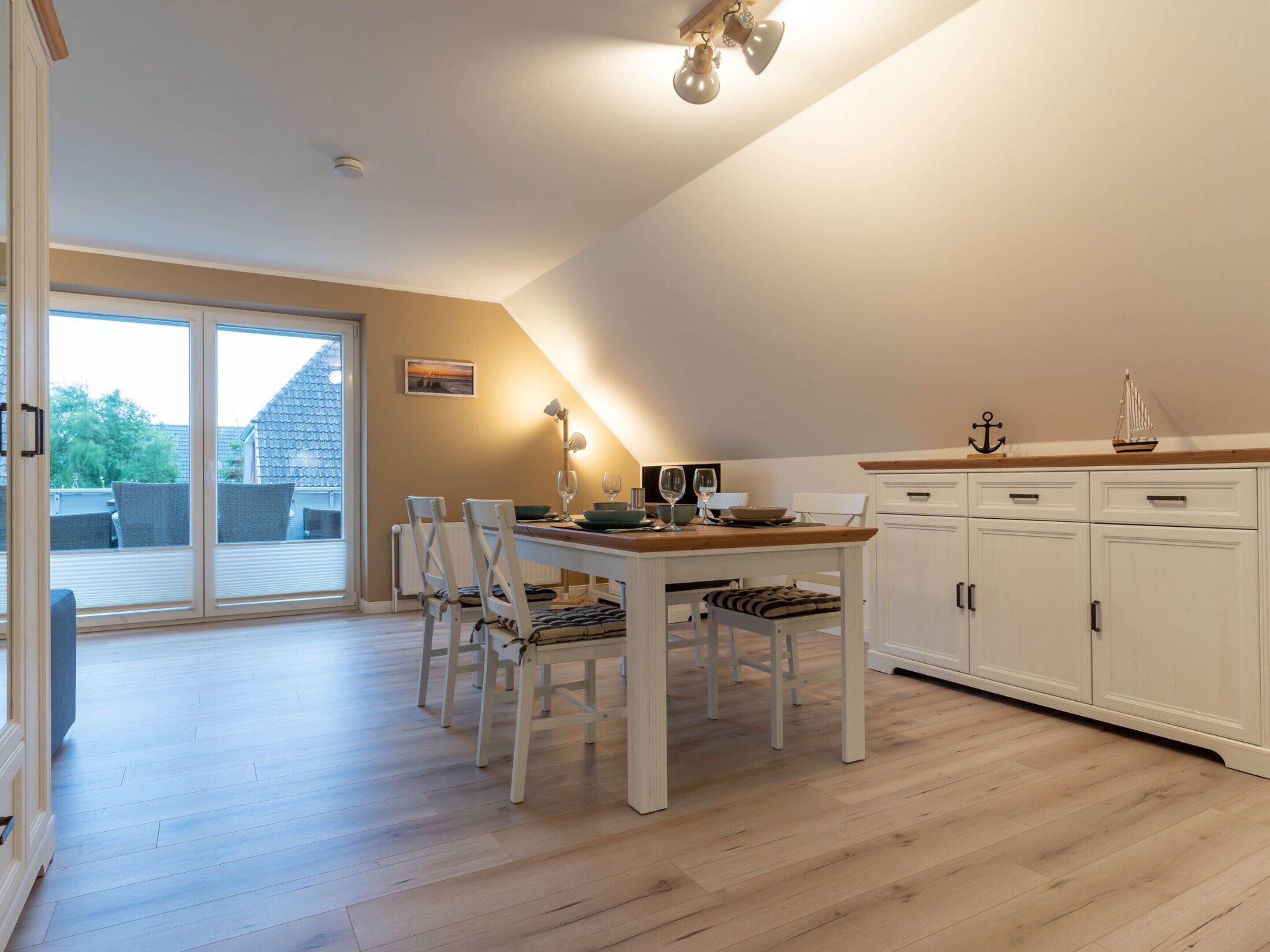 A spacious room with a dining table, chairs, a kitchen area, and a sliding glass door leading to an outdoor patio.