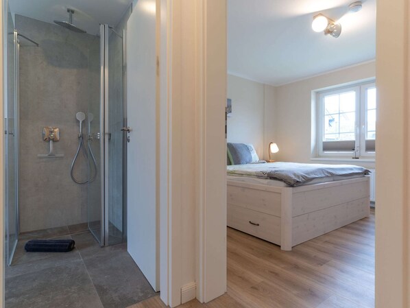 Une chambre moderne équipée d’une douche, d’un lit avec une table de chevet et d’une fenêtre laissant entrer la lumière naturelle.