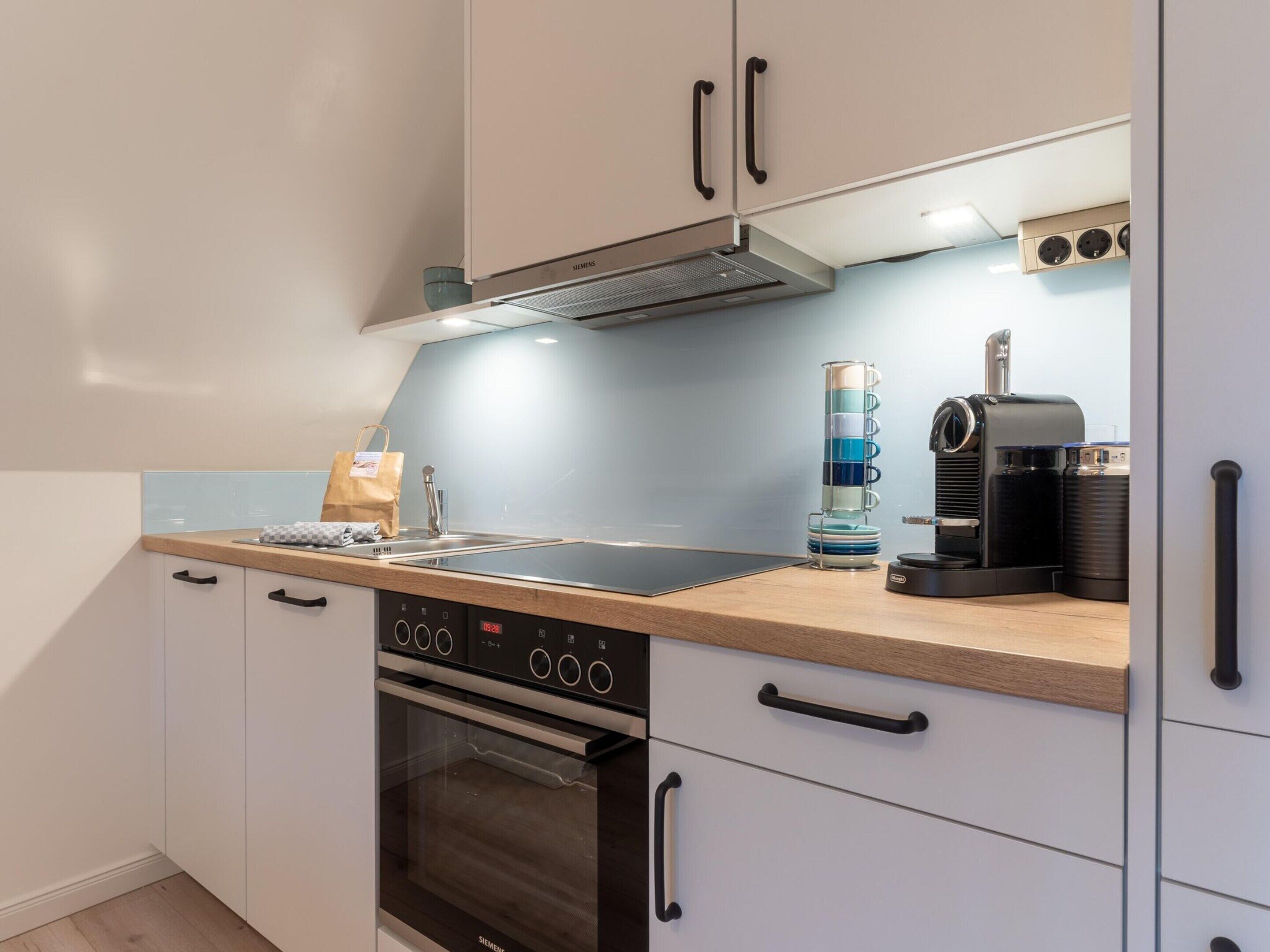 Une cuisine moderne avec des armoires blanches, une hotte de cuisinière en acier inoxydable, un four encastré et une machine à café.