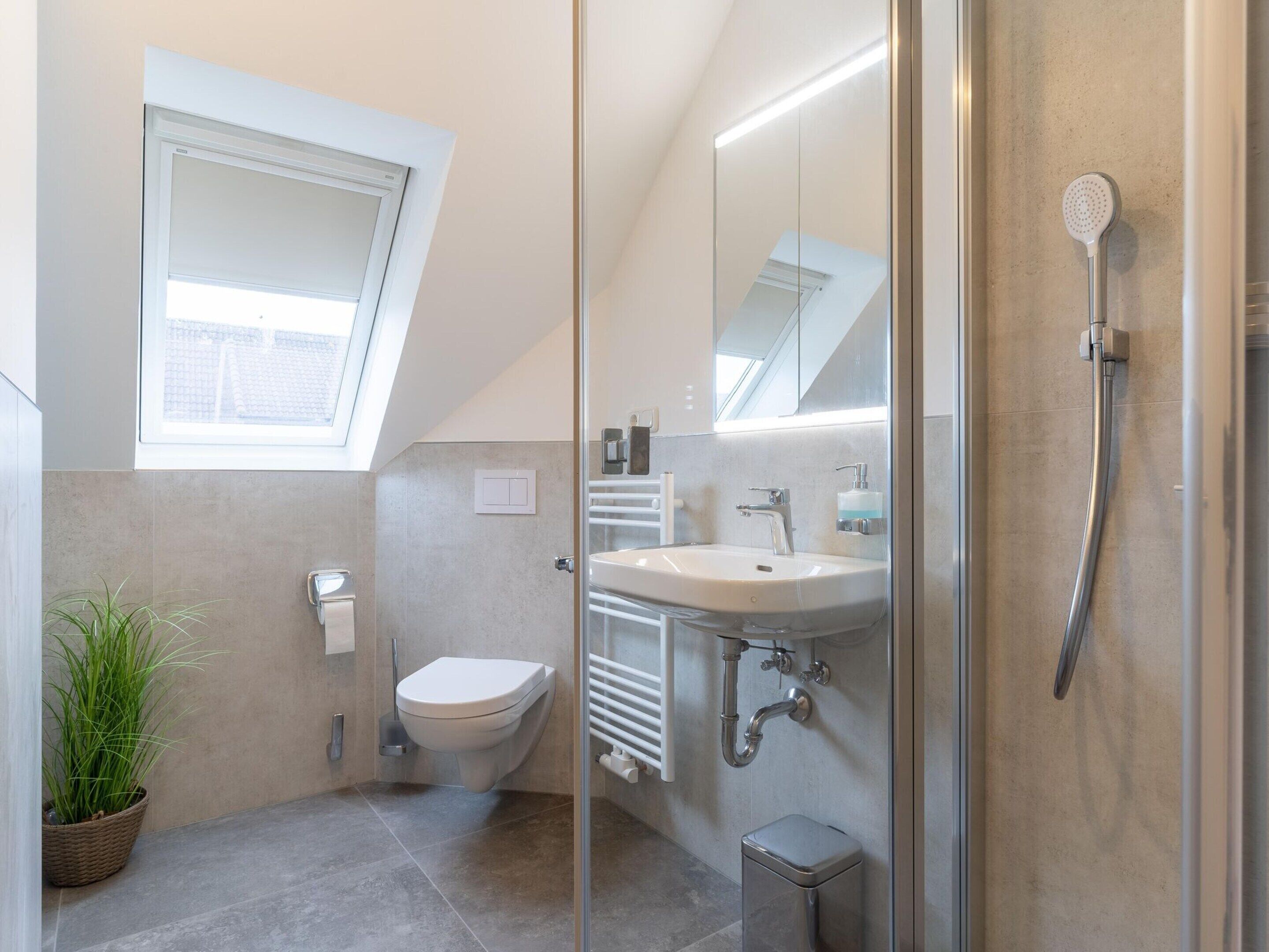 Ein modernes Badezimmer mit Dachfenster, Toilette, Waschbecken und Dusche.