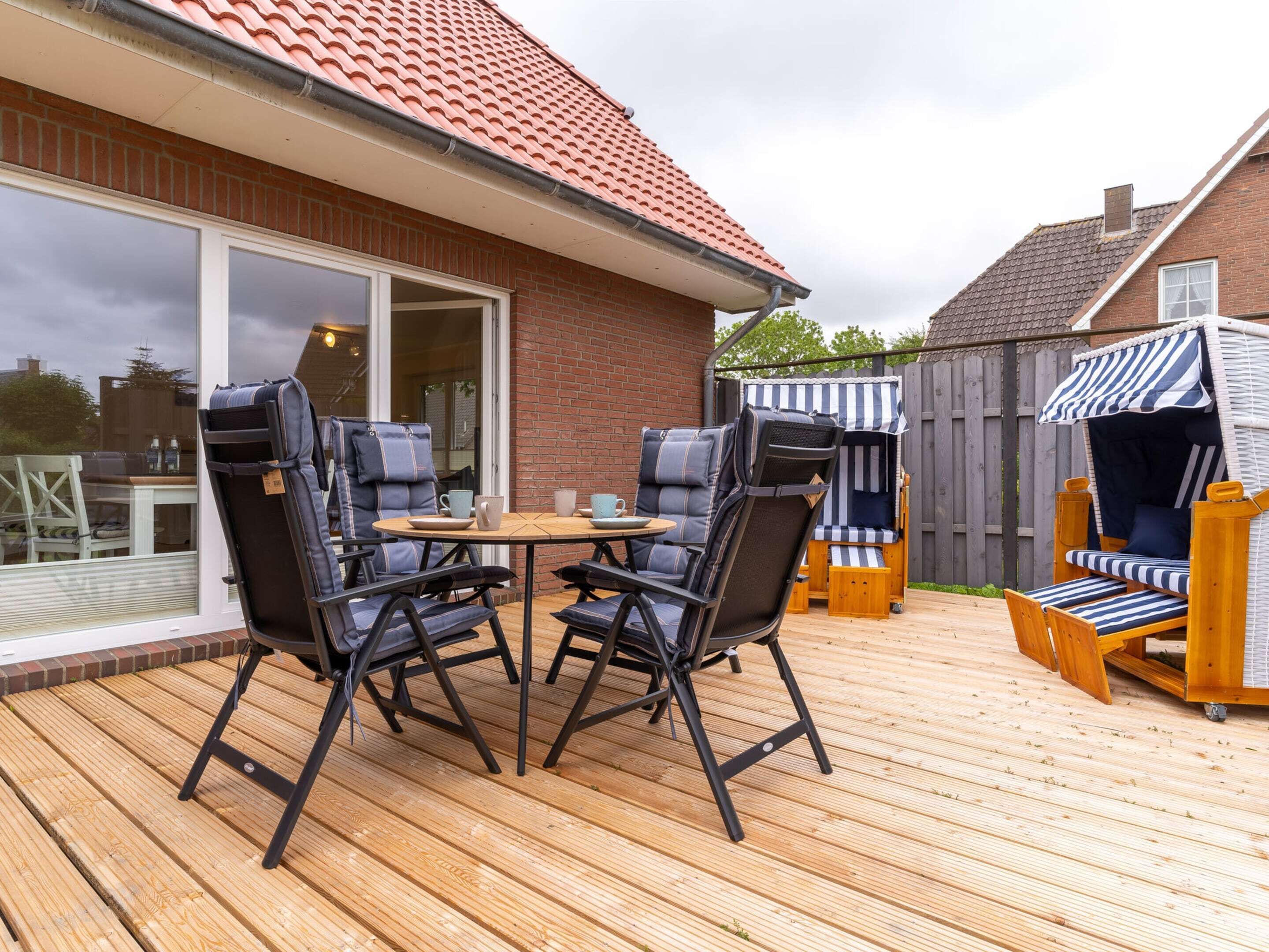 An outdoor patio with a wooden deck, two black folding chairs, a small round table, and a striped beach chair.