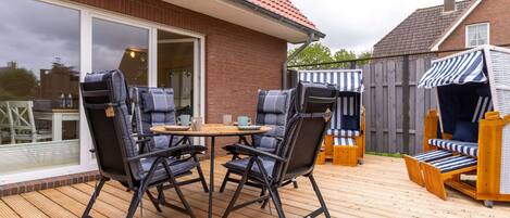 An outdoor patio with a wooden deck, two black folding chairs, a small round table, and a striped beach chair.