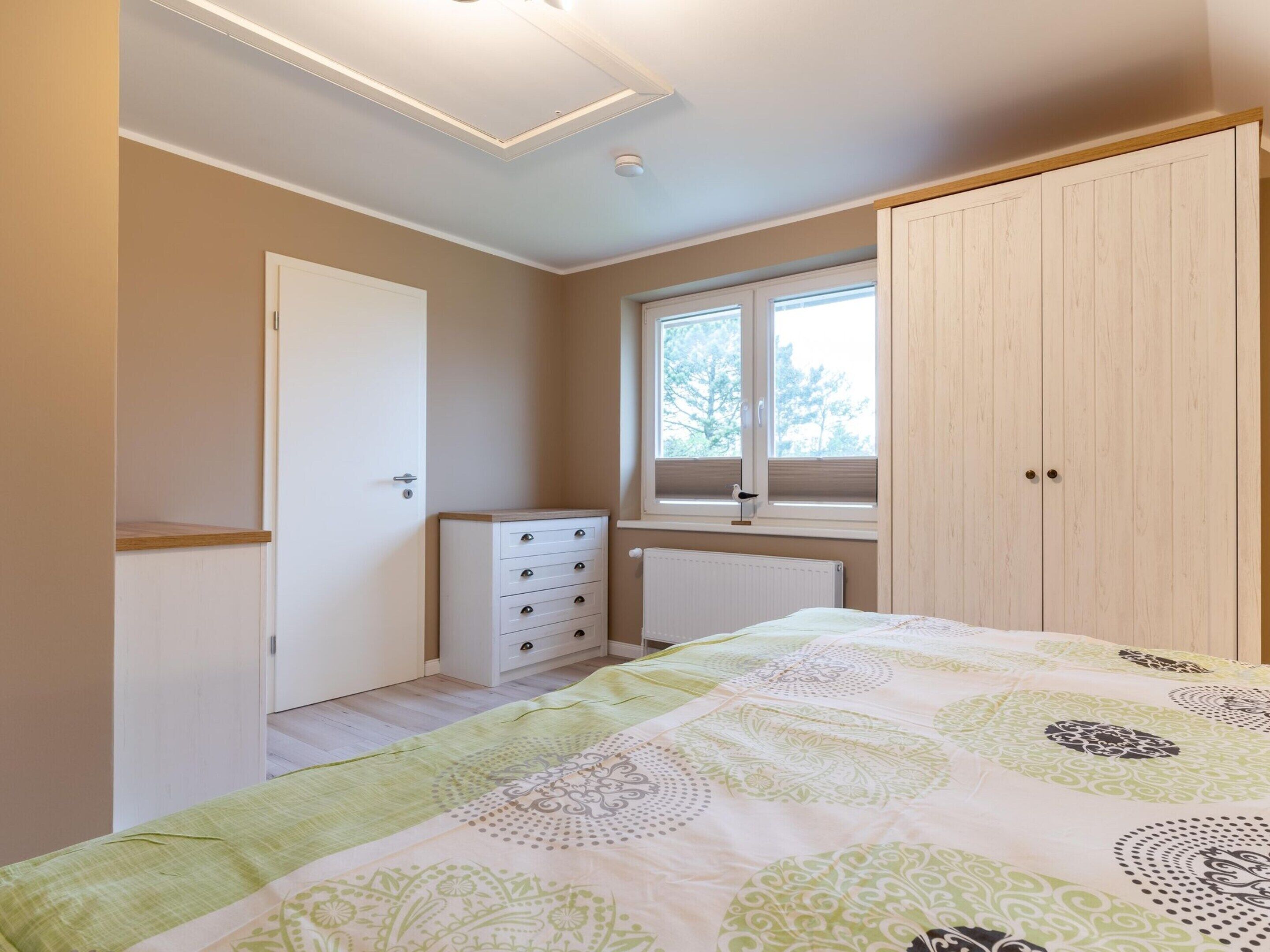 Un dormitorio con cama, cómoda, armario, ventana y radiador.