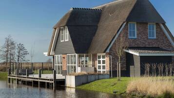 A house with a steeply pitched roof, large windows, and a dock extending into a body of water.