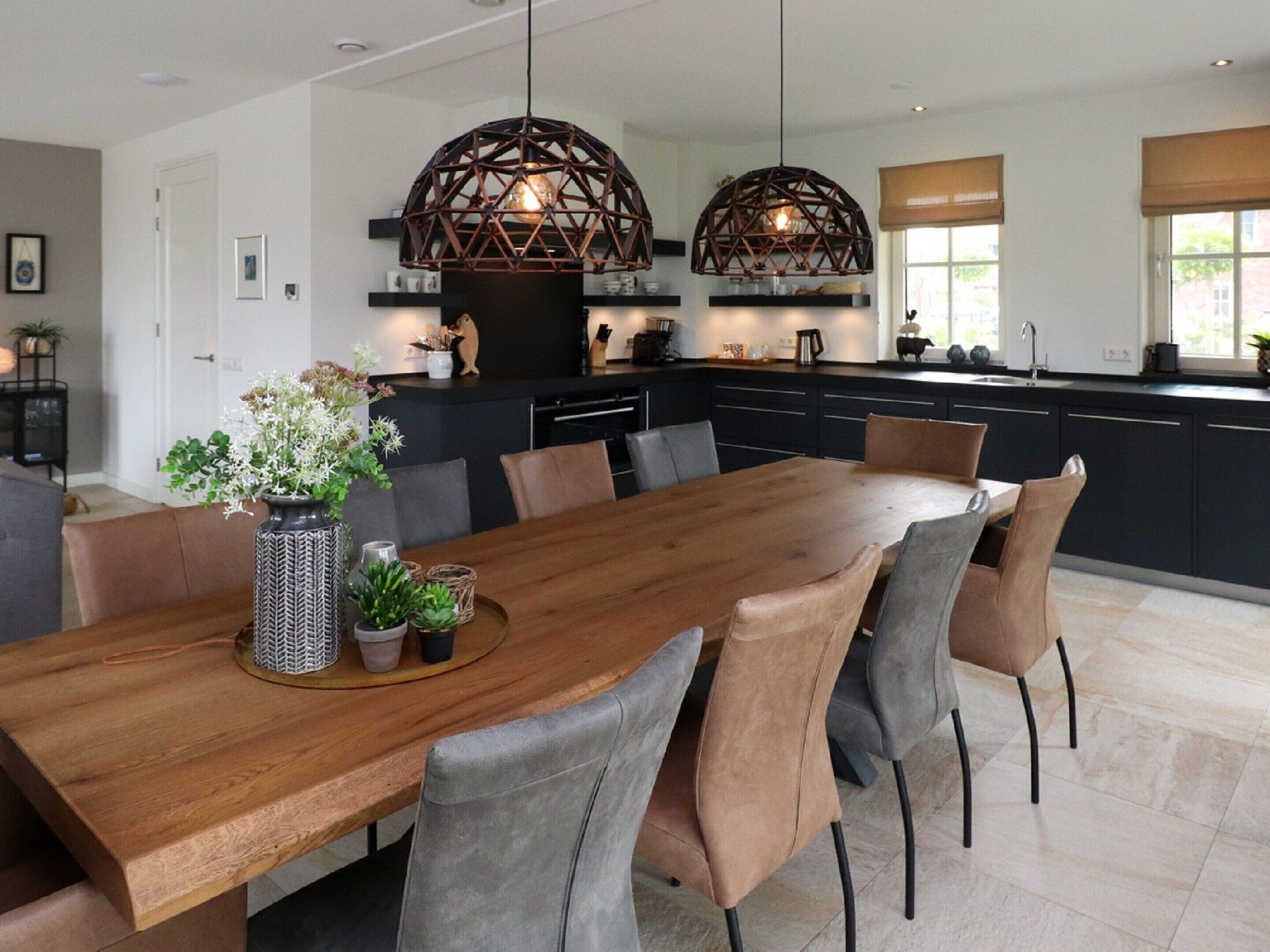 A modern kitchen with dark cabinetry, a wooden dining table, and pendant lights.