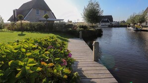 A canal-side property with a wooden dock leading to a house with a thatched roof. - Luxury Villa With a Sauna, at the Tjeukemeer (Delfstrahuizen)