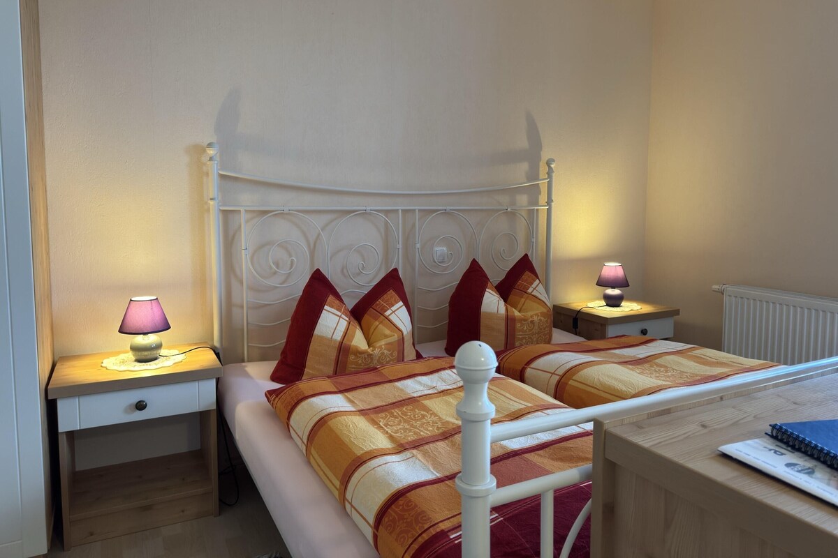 A neatly arranged bedroom with a bed, two bedside tables, and a small desk.
