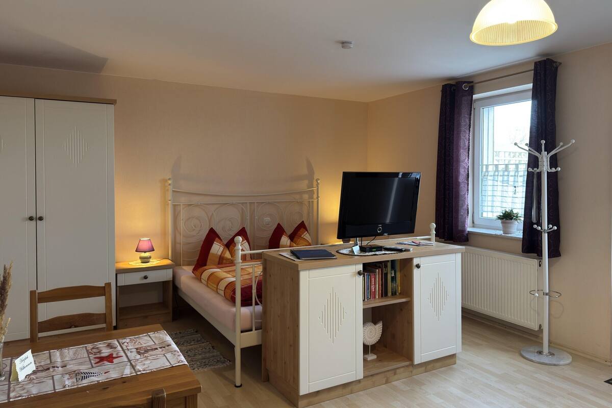 Quarto com cama, mesa de cabeceira, luminária, televisão, guarda-roupa e janela com cortinas.