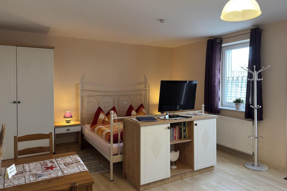 A bedroom with a bed, bedside table, lamp, TV, wardrobe, and a window with curtains.