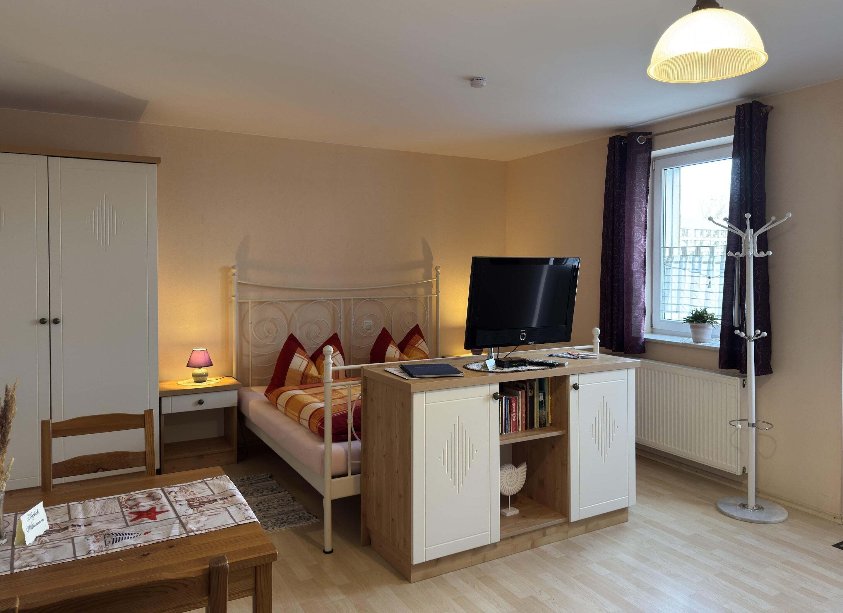 A bedroom with a bed, bedside table, lamp, TV, wardrobe, and a window with curtains.