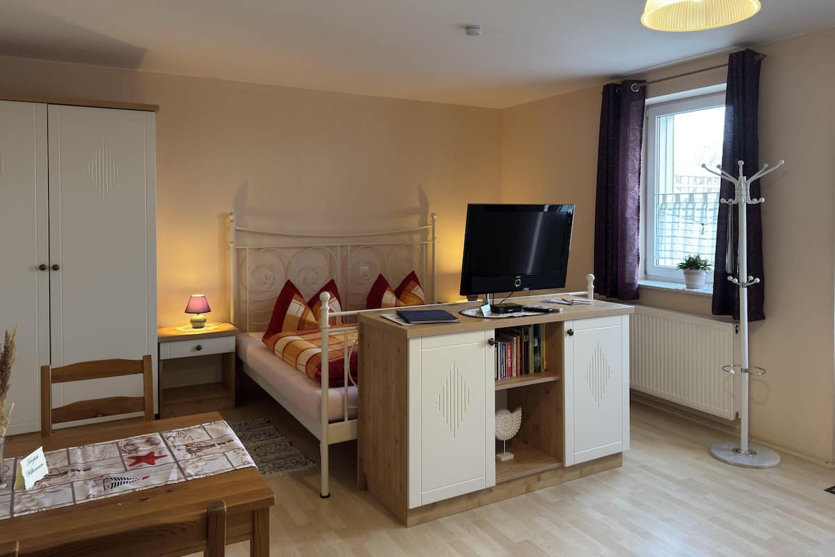 A bedroom with a bed, bedside table, lamp, TV, wardrobe, and a window with curtains.